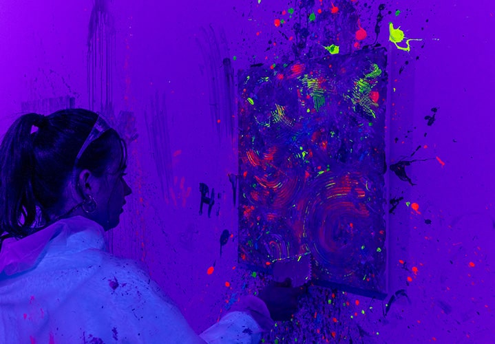 A woman using a pattern scraper on a canvas in UV light