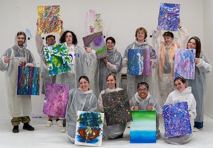 A group of 11 people showing their painted canvases